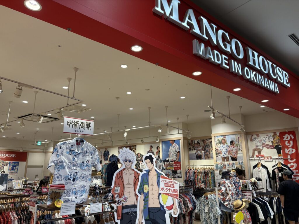 「MANGO HOUSE MADE IN OKINAWA」の赤い看板が目を引く店舗風景。右側には「かりゆしウェア」ののぼりがあり、店内には色鮮やかなシャツが多数陳列されている