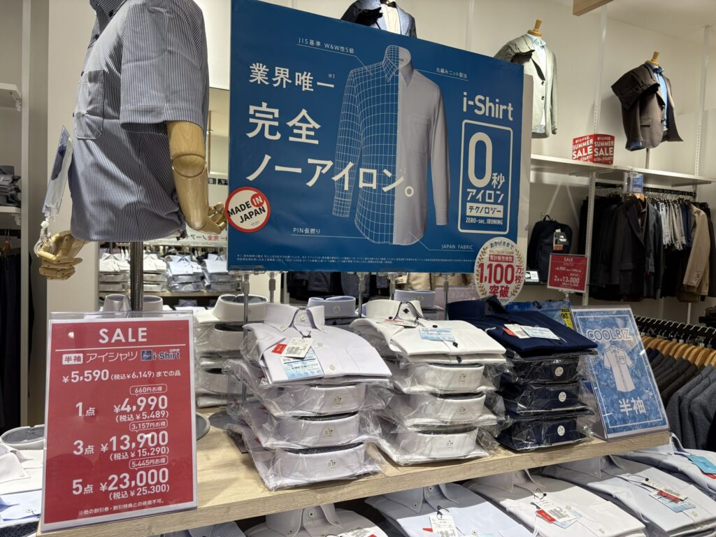 「業界唯一 完全ノーアイロン。0秒アイロンテクノロジー」と大きく書かれたi-Shirtの店頭POPと、陳列されたシャツの写真　半袖のi-Shirtが1点4,990円、3点13,900円、5点23,000円（税抜）でまとめ買いセールされている店頭の様子